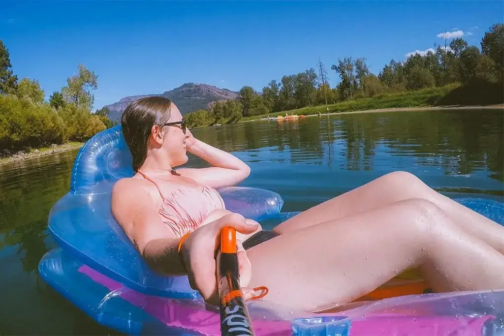 Selfie of a woman on a floatie on the Enderby River with the Enderby Cliffs in the background.