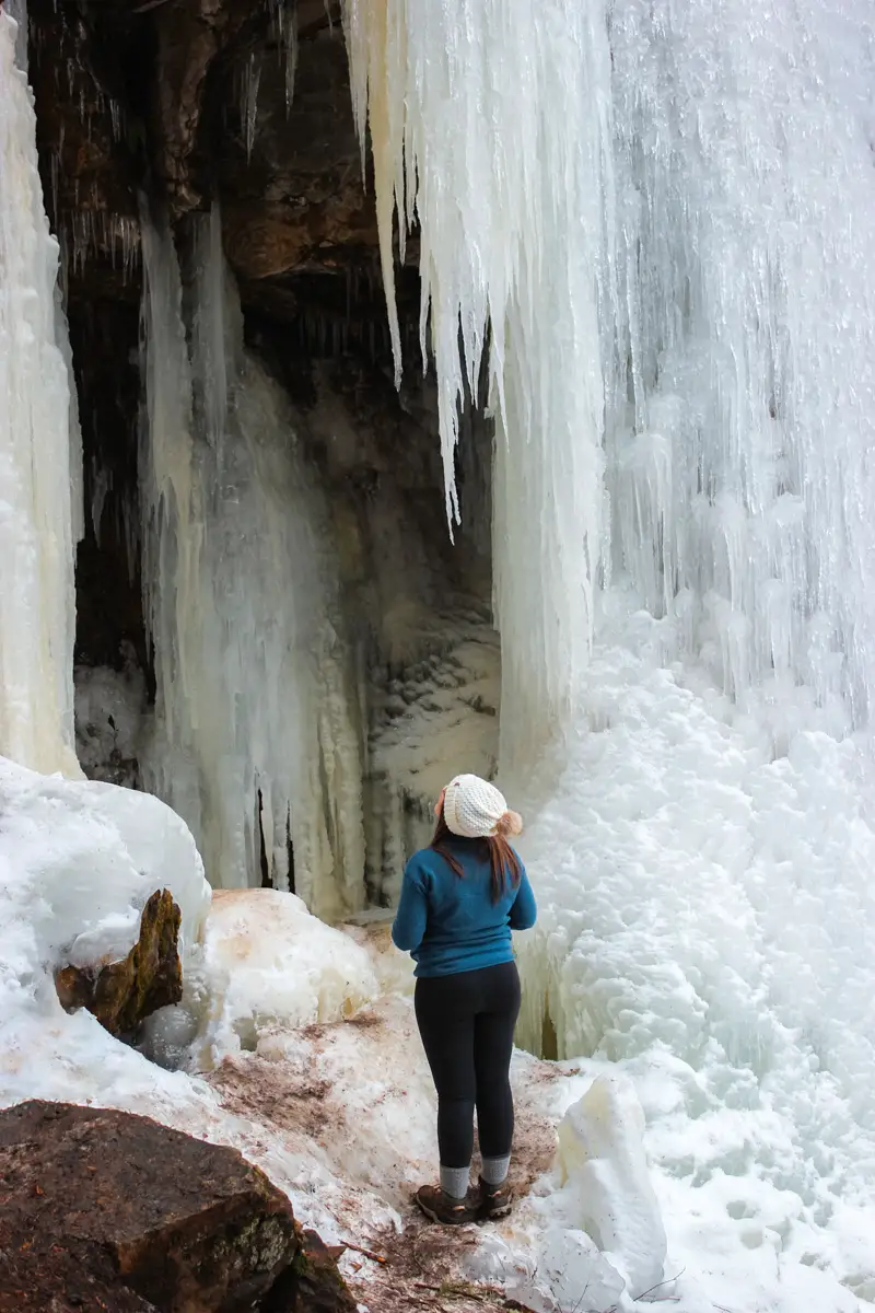 Women stands under the frozen Cosesns Falls, looking at an icicle.