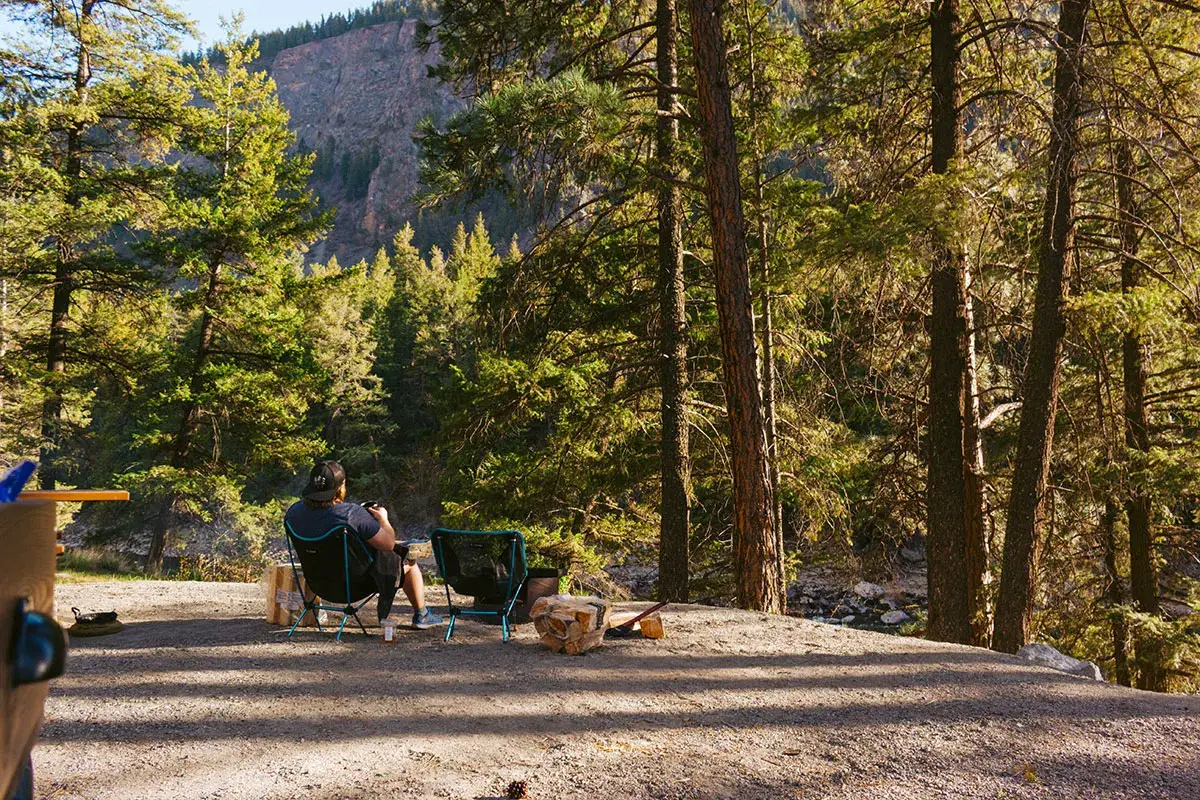 Man sits on small camping chairs in a campsite in BC.