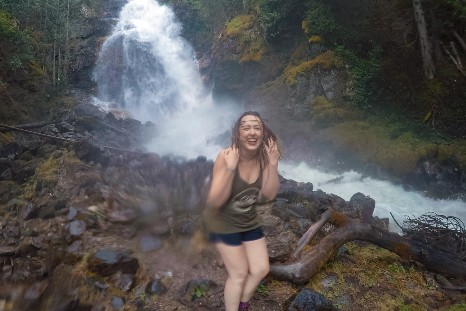 Woman stands in front of Kay Falls, laughing because her hair is being whipped around by the strong winds