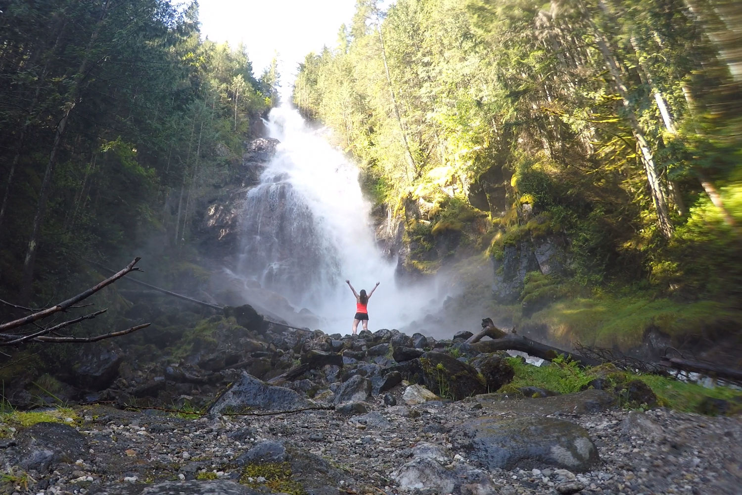 Woman stands with arms up in front of Kay Falls on a sunny day