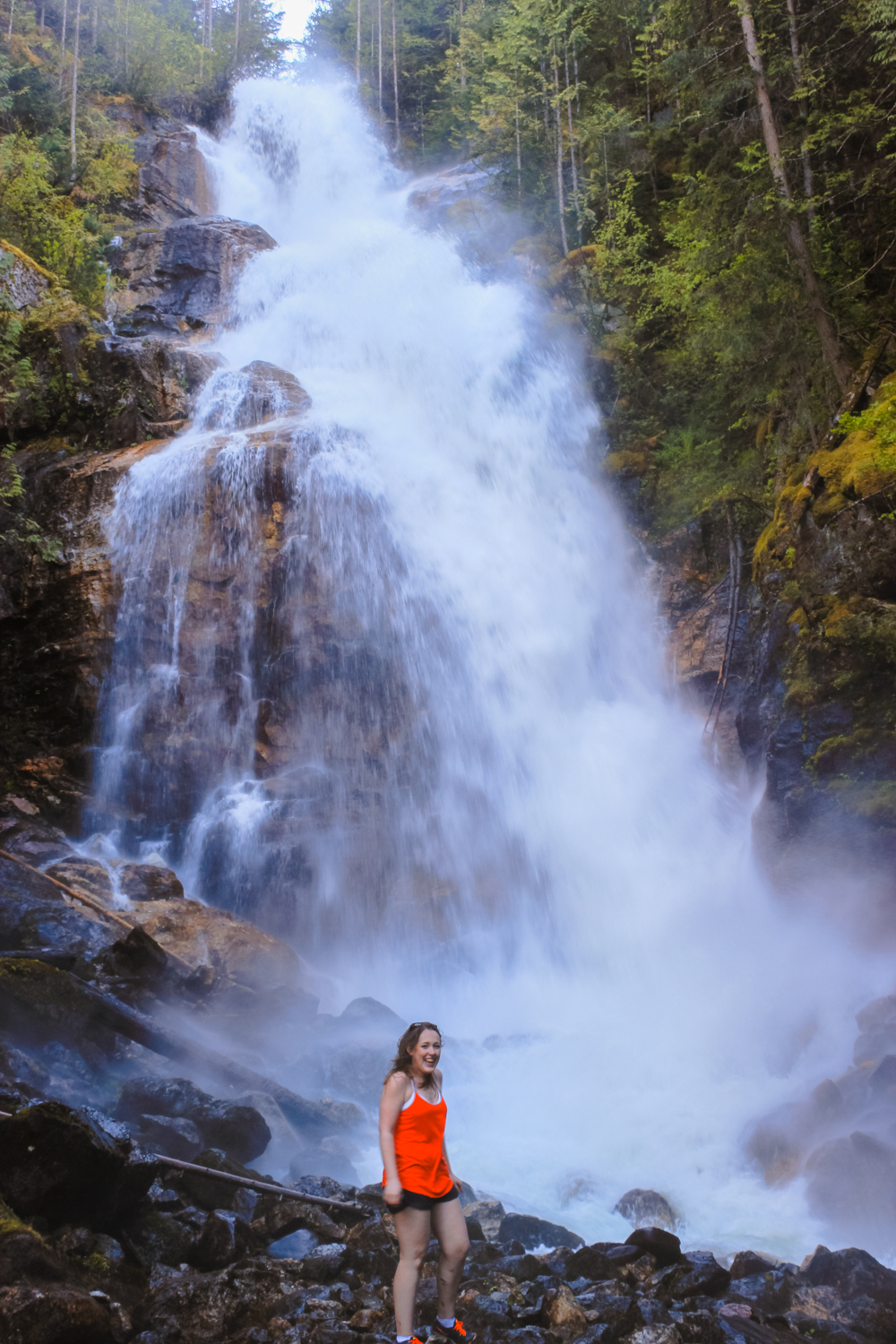Woman in red stands in front of Kay Falls as it rushes down in the spring