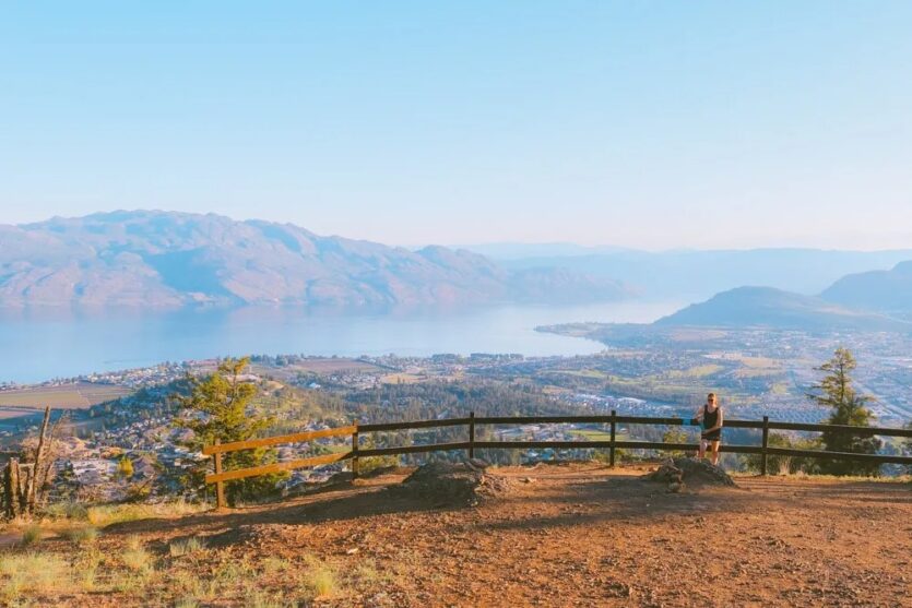 Woman standing at the summit of Mt Boucherie hike in West Kelowna, overlooking Okanagan Lake.