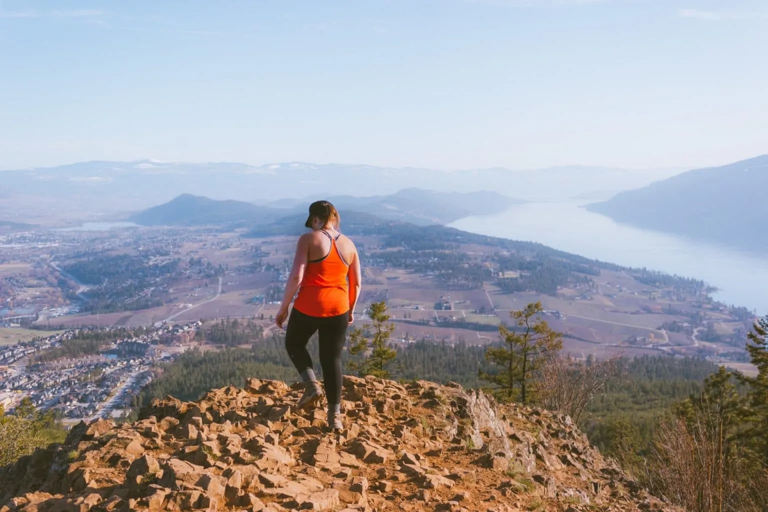 Woman standing at the top of Spion Kop hike overlooking Lake Country and Okanagan Lake.