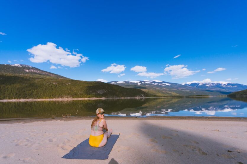 Woman in bathing suit sits on a towel on a sandy beach on Arrow Lake.