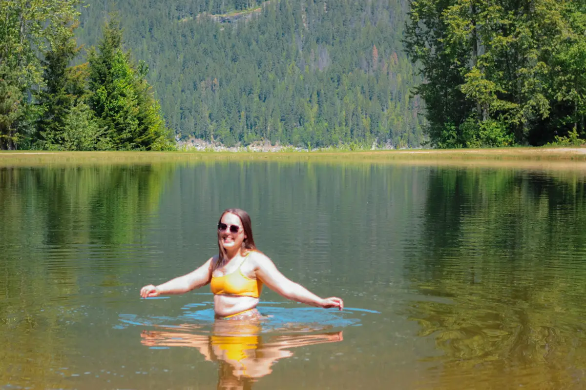 Woman in yellow bathing suit in a small swimming lagoon at Blanket Creek, surrounded by trees.