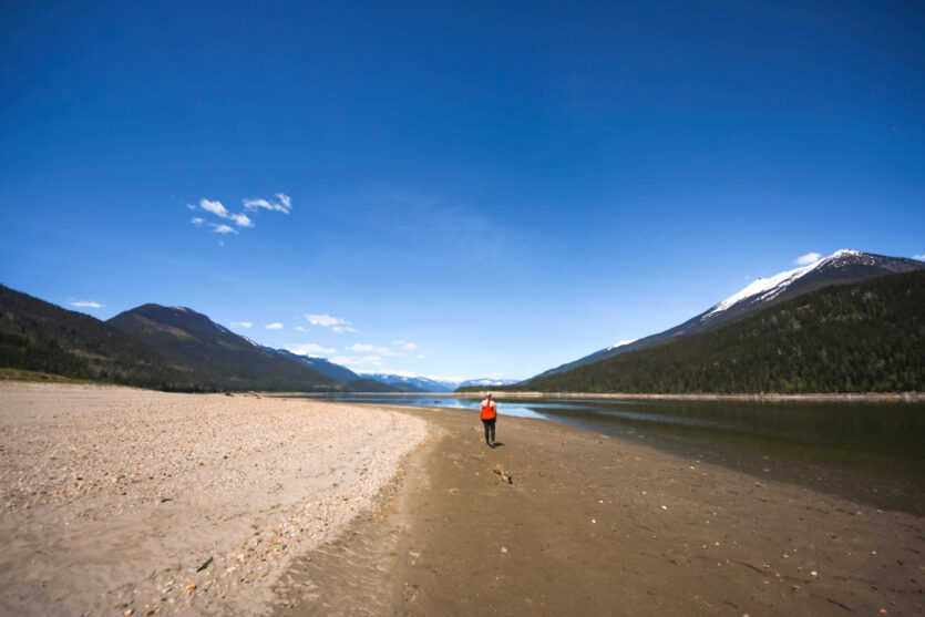 Woman walks down a large sandy beach in Revelstoke