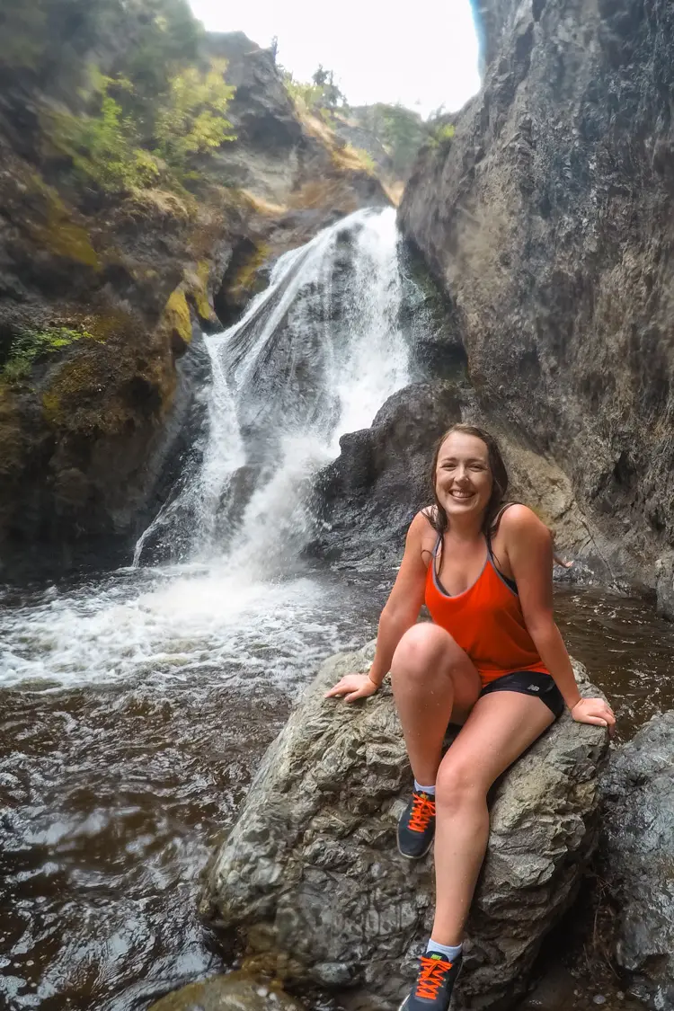 Woman in red sits in front of Bear Creek waterfall in Kelowna, BC