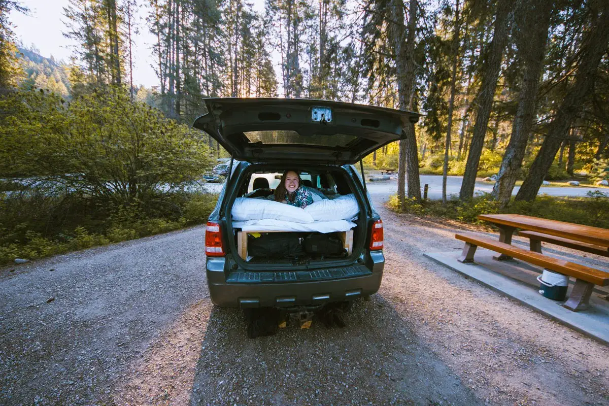 Woman lays in the back of a Ford Escape SUV converted for camping