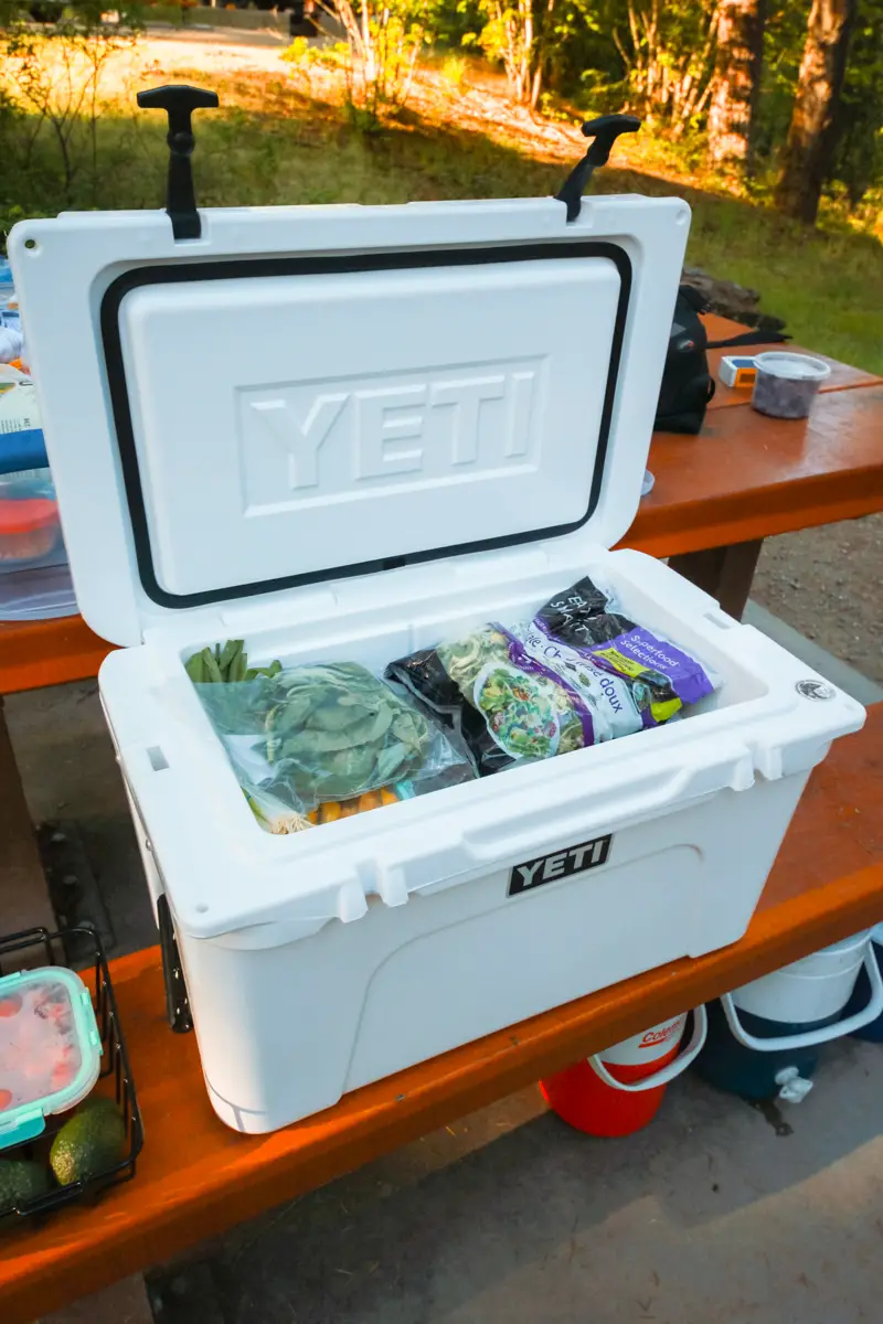 White Yeti cooler sits on a picnic table, open and full of food