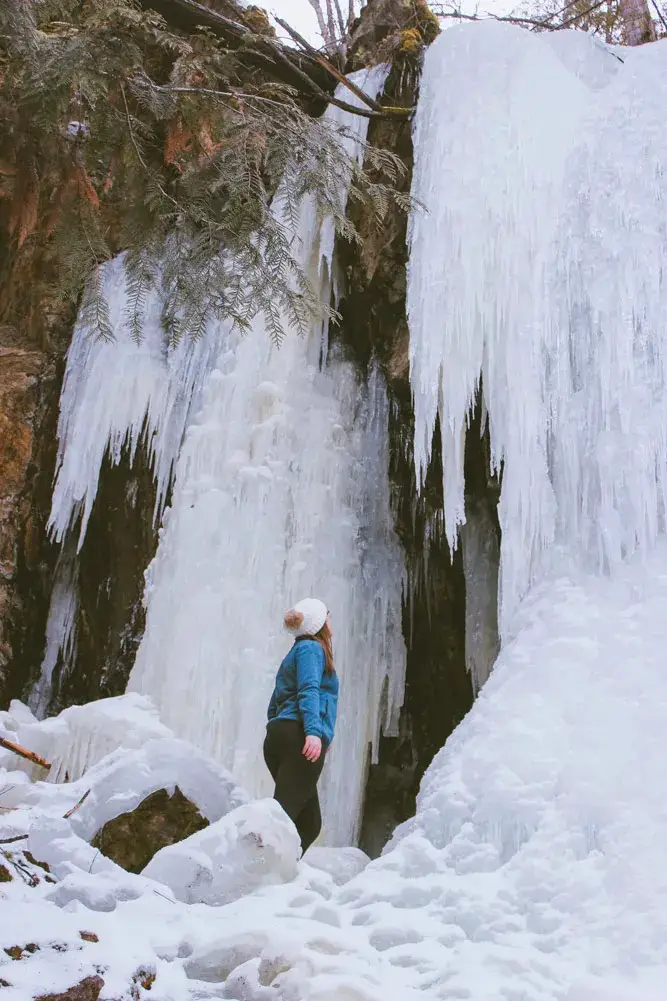 Woman stands in front of a frozen waterfall in Vernon