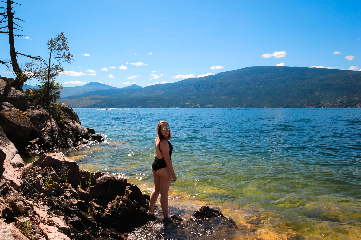 Woman stands on the shore of a beautiful blue lake ready to go swimming
