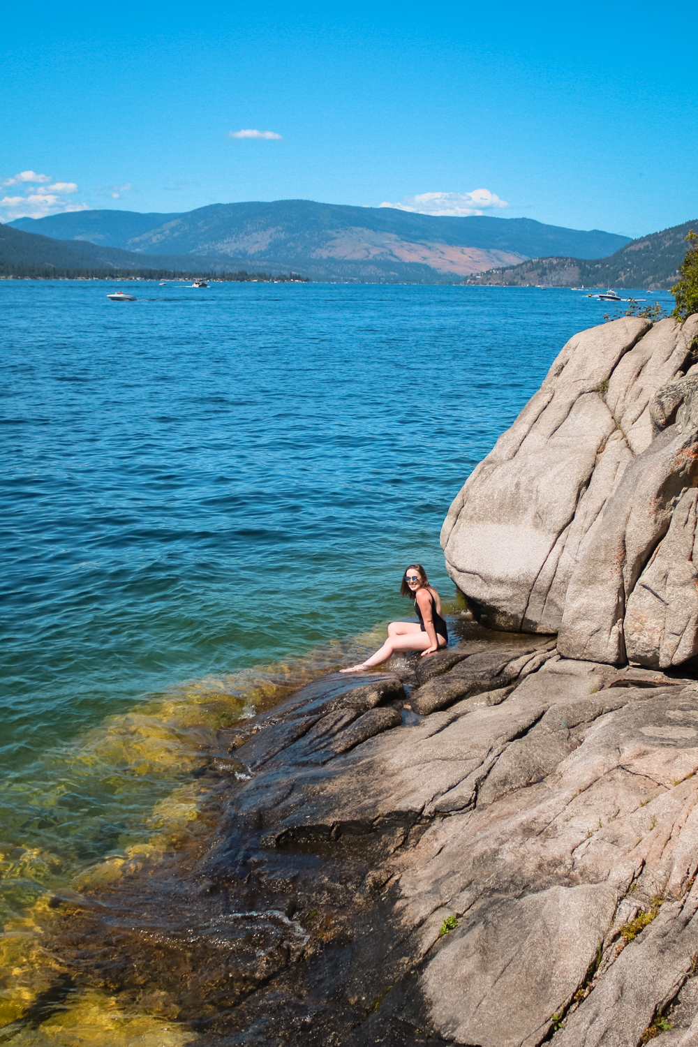 Woman sits on the rocks next to a crystal clear blue lake
