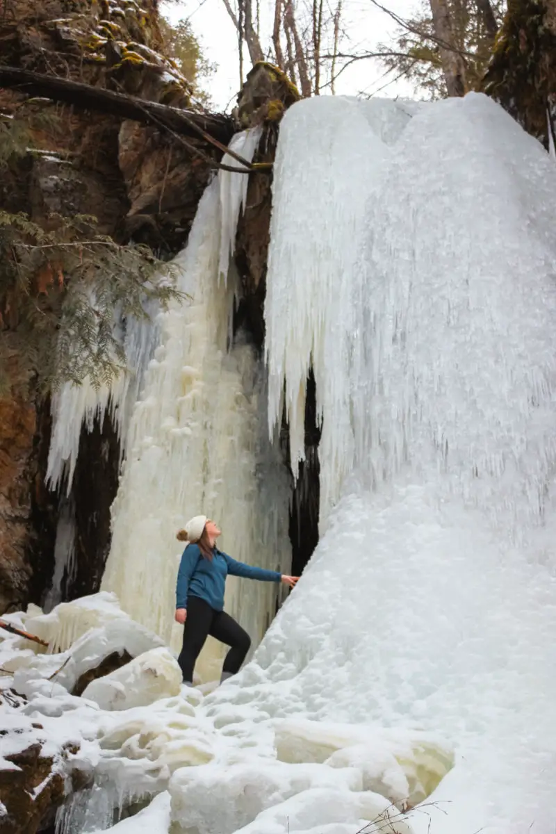 Woman stands at the base of a frozen waterfall