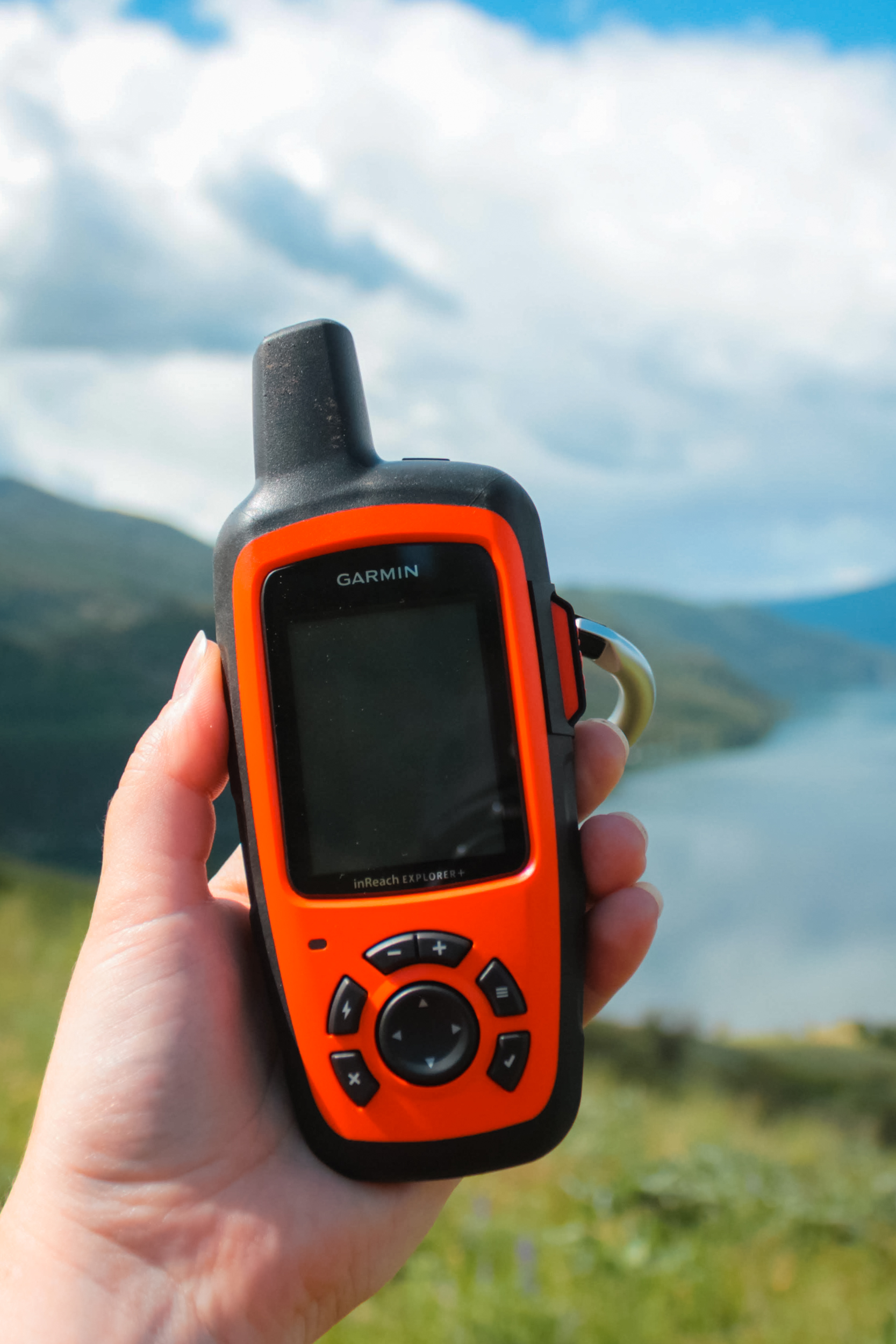 Women holds Garmin Inreach Explorer GPS with Kal Lake in the background