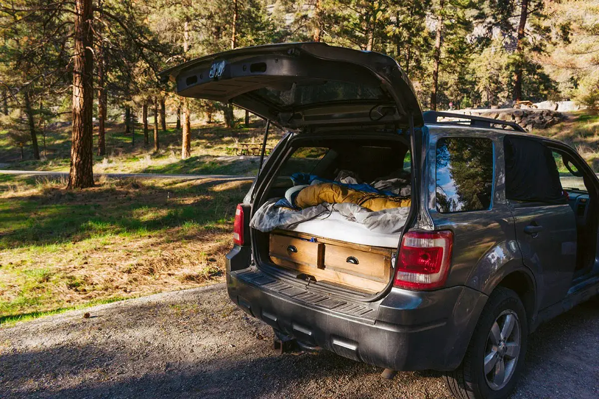 SUV with open hatch that's set up for car camping with blankets, pillows, and drawers