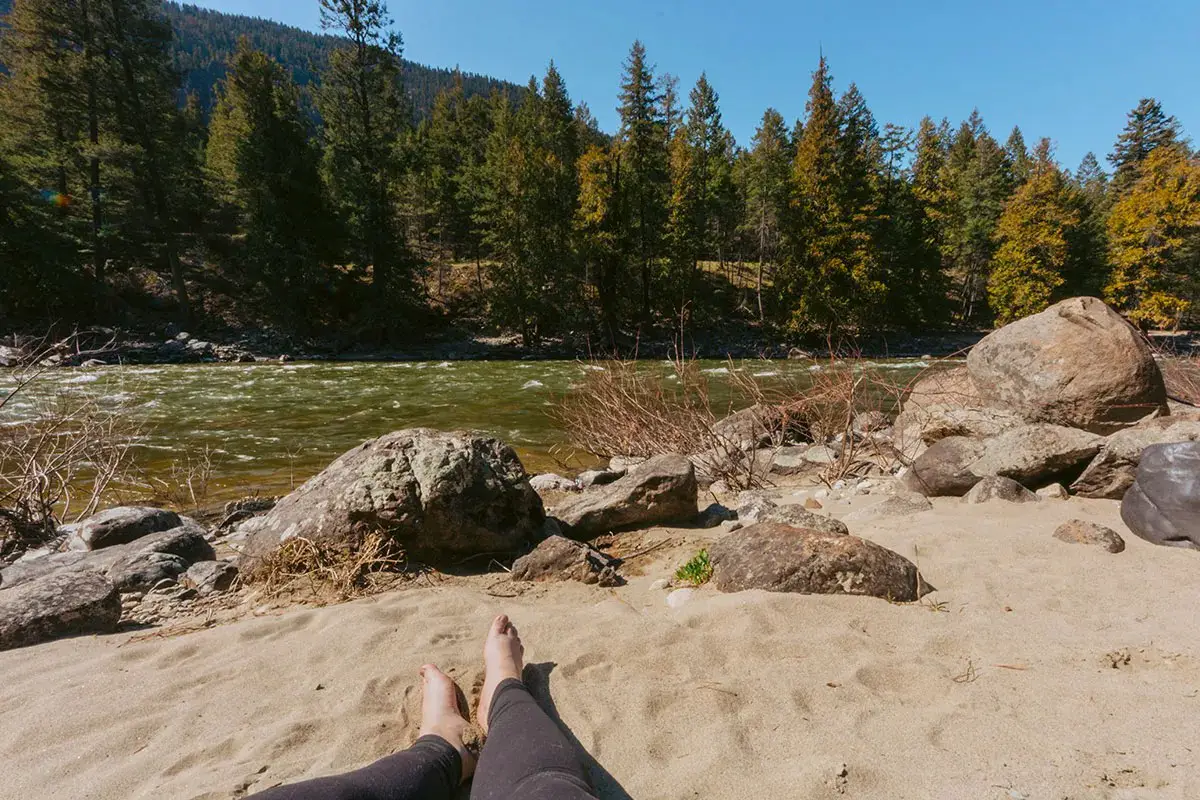 Person sits on a sandy beach next to a river
