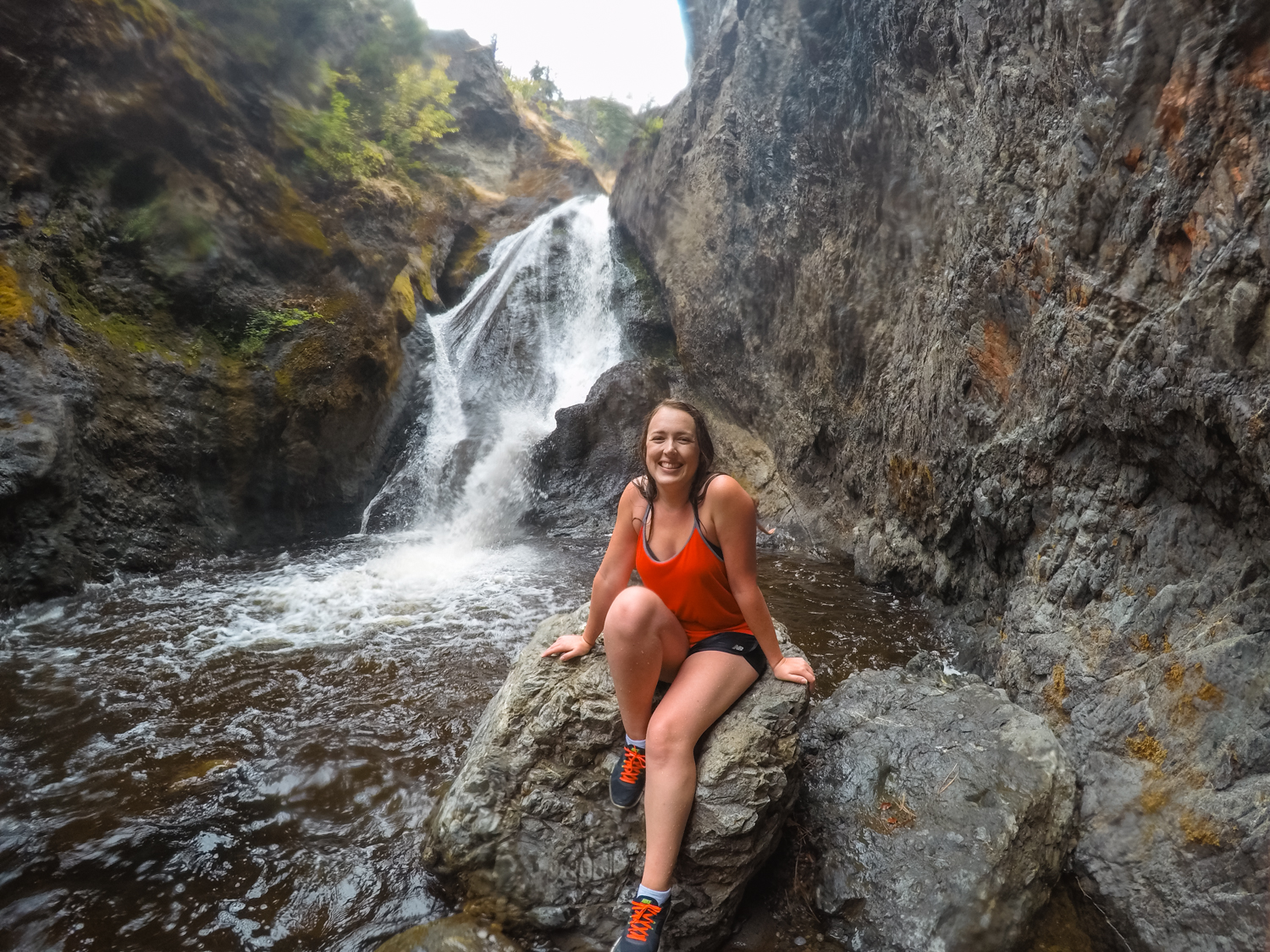 Woman in red sits on a rock in front of a canyon waterfall.