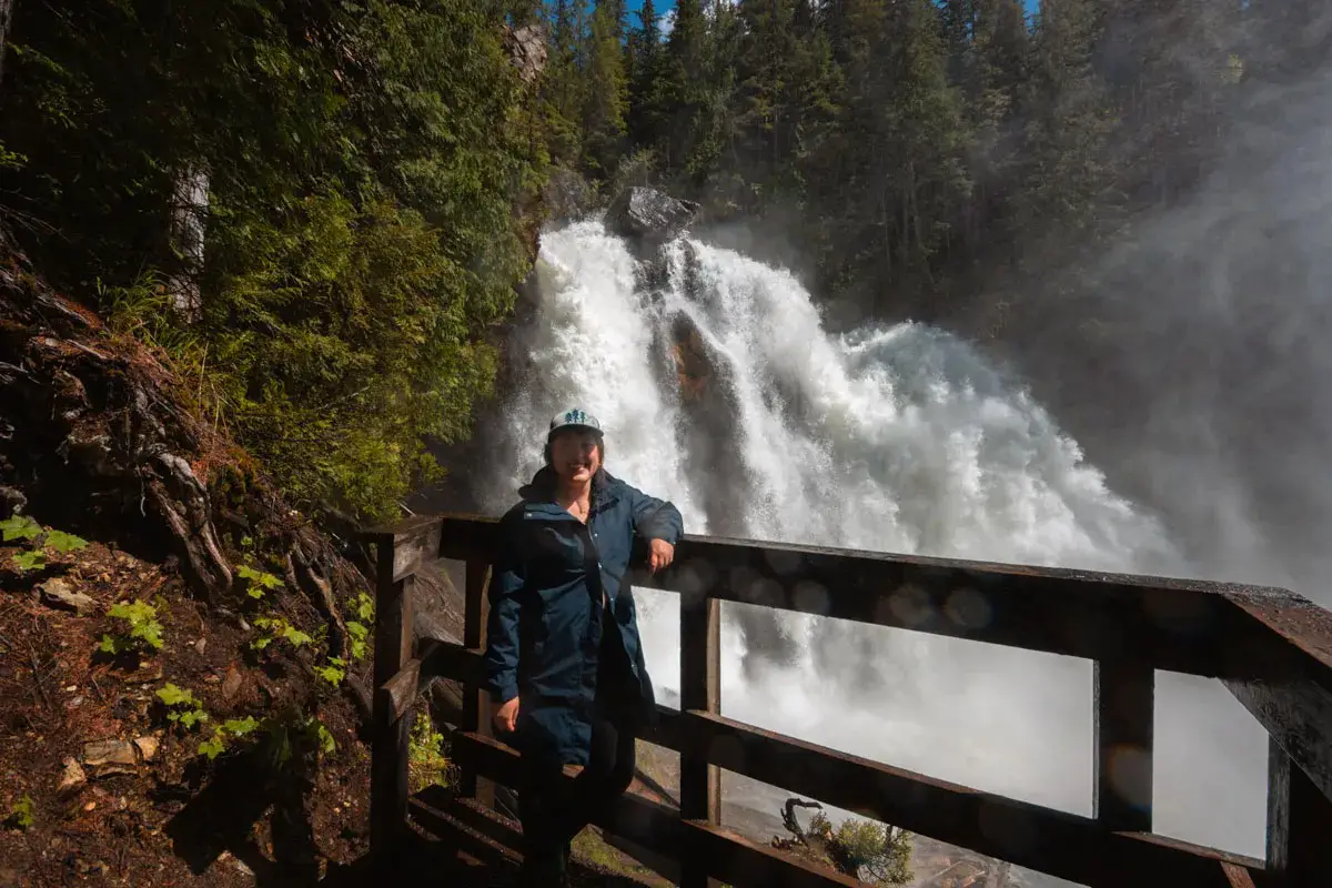 Woman wearing a hat and rain jacket stands in front of Rainbow Falls in the Monashee Mountains