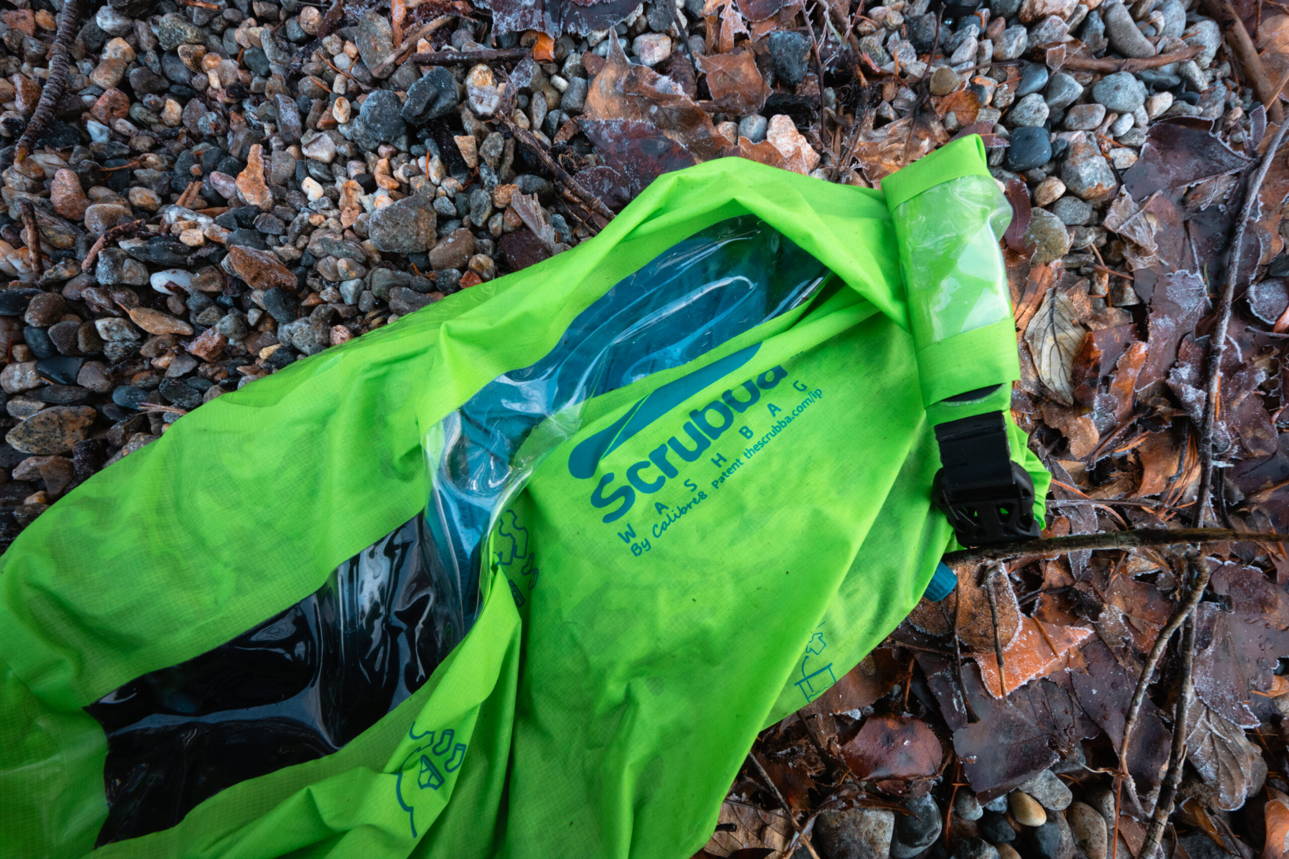 Green Scrubba wash bag filled with clothes on a rocky shorline.