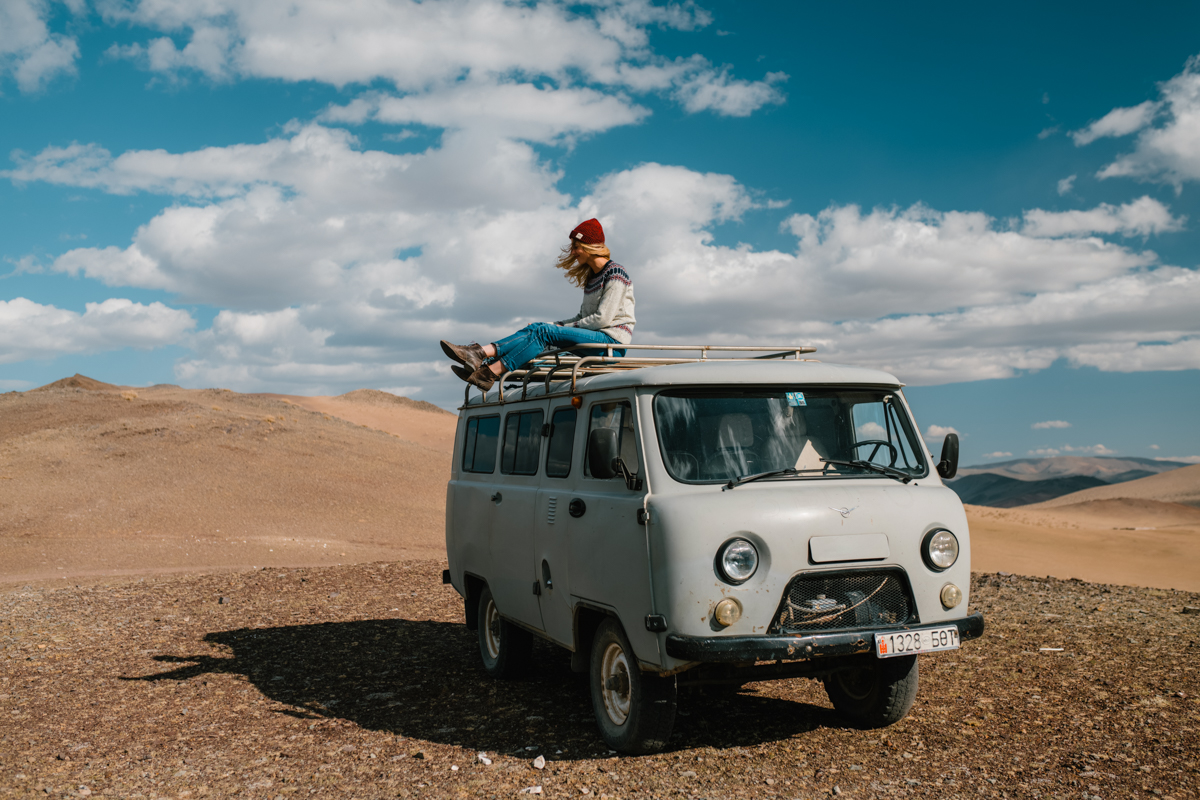 Woman sites on top of a vintage van while on a road trip.