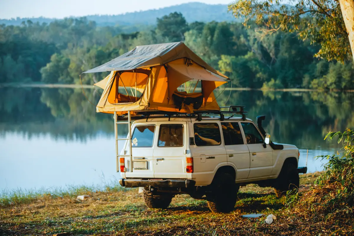 Rooftop tent on a jeep next to a lake.