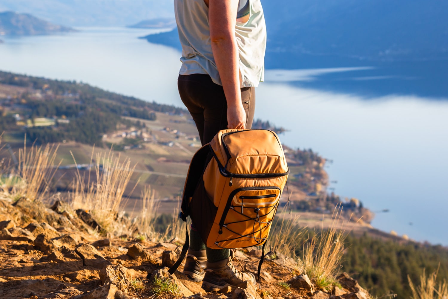 Woman holds the EVERFUN 30-can Cooler Backpack at the top of a mountain.