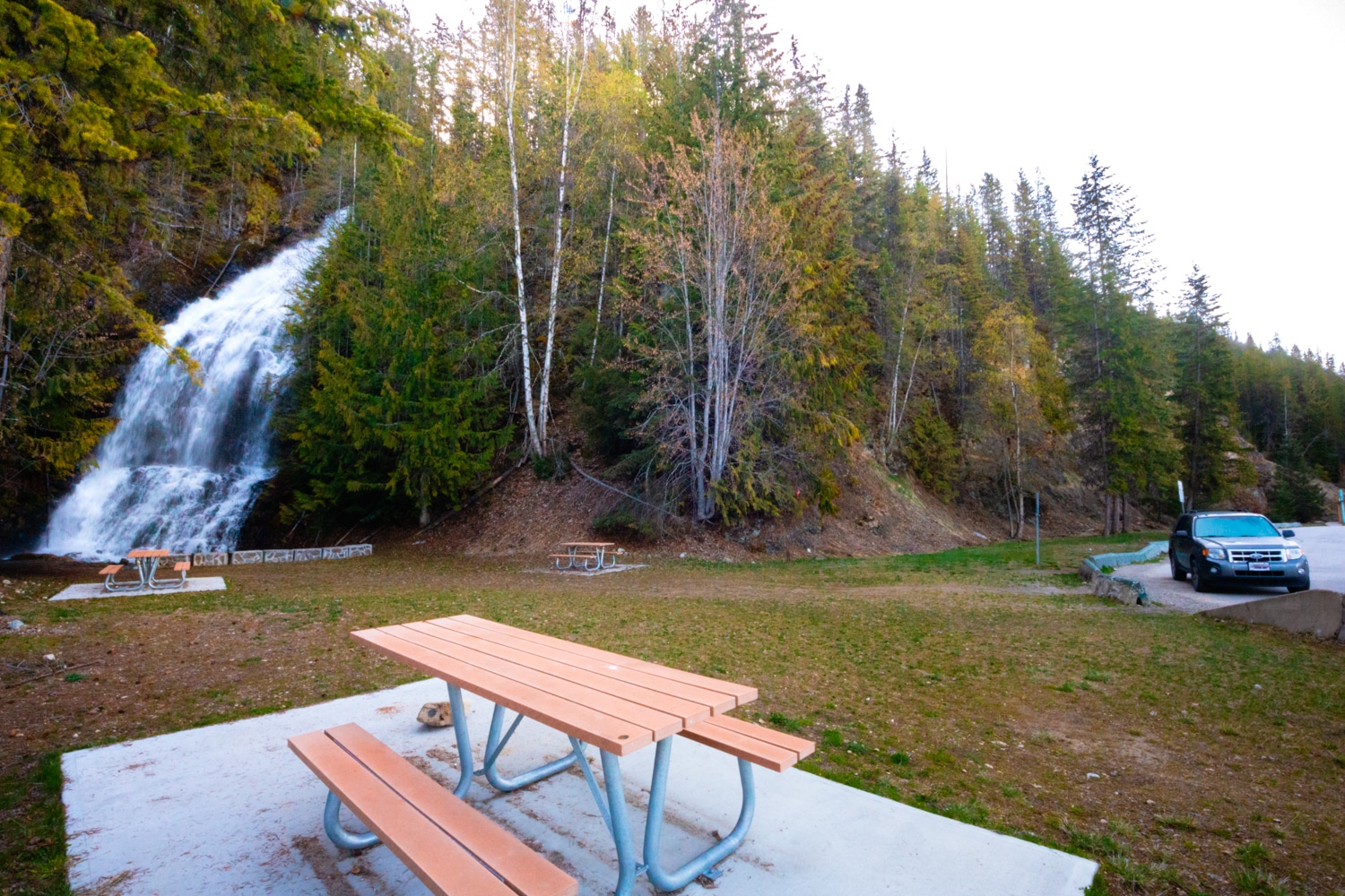 View of the picnic area, parking area, and waterfall at the Ione Rest Area near Nakusp, BC.