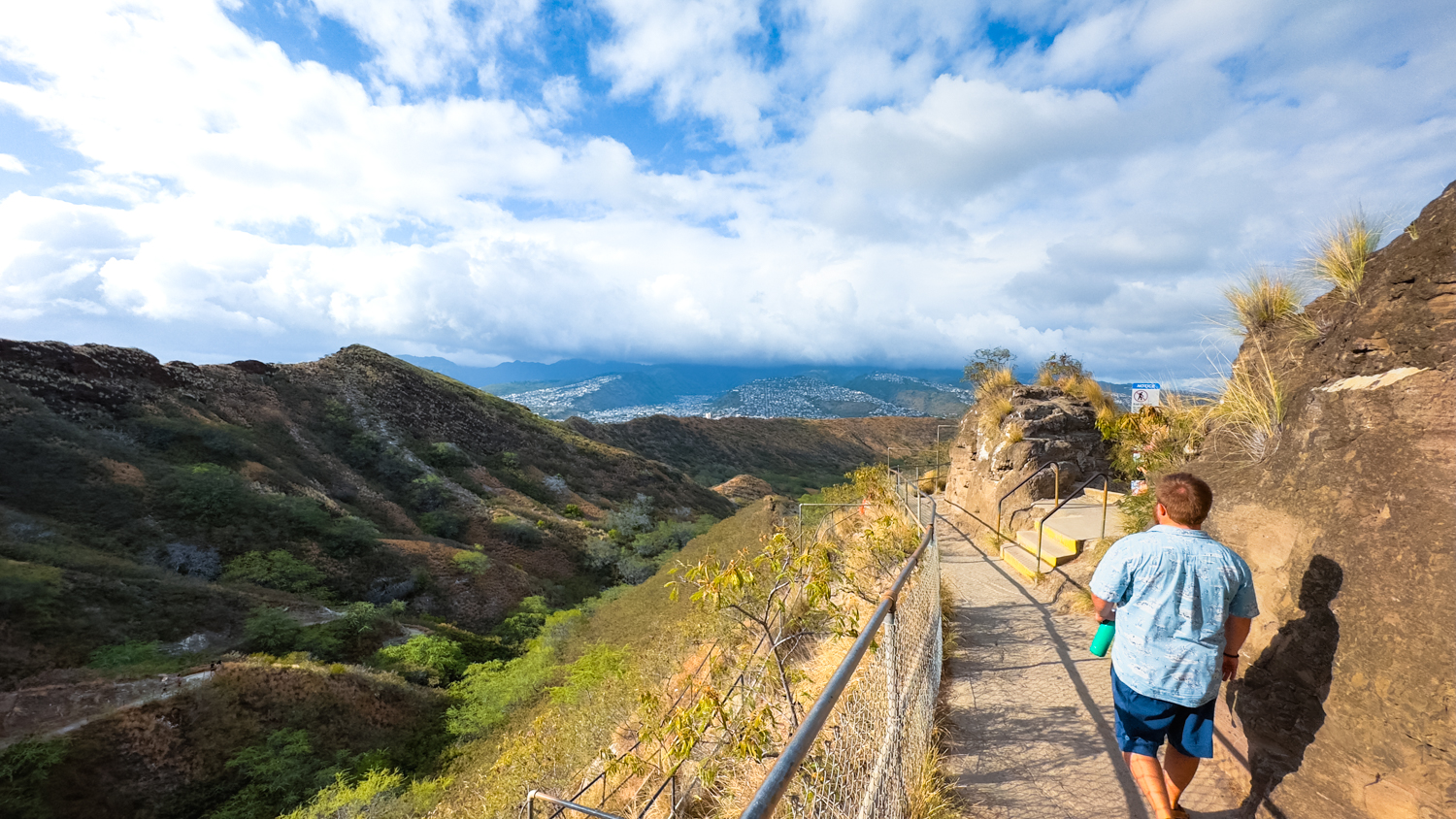 Man walks along the trail overlooking the crater walls of Diamond Head with Honolulu in the distance.