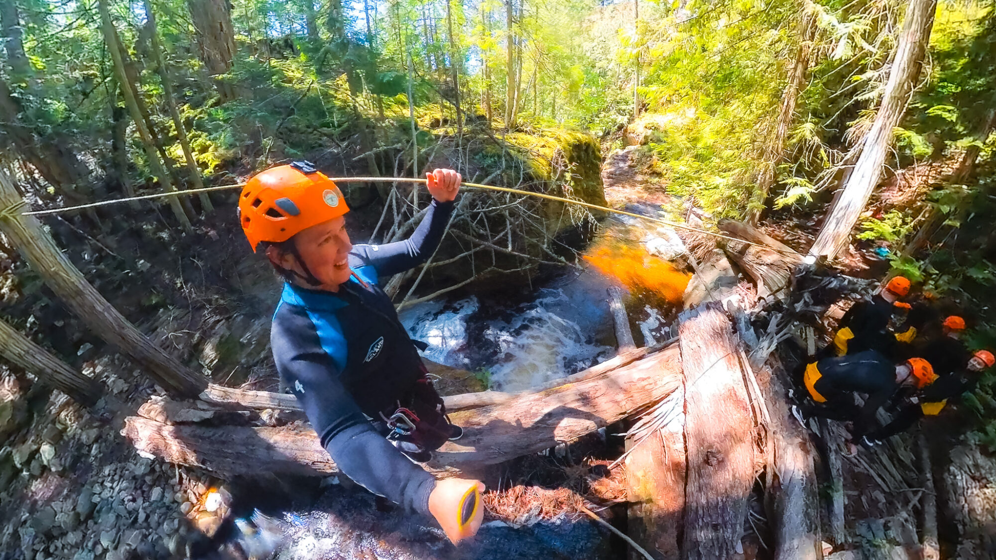 A woman walks over a fallen log while connected to a rope