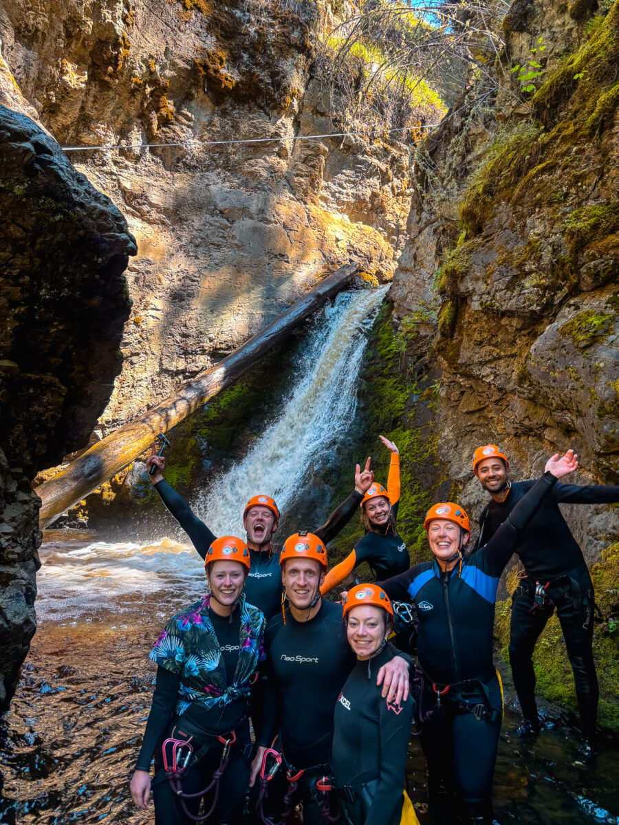 A group of excited people stand in front of a waterfall that they ziplined down