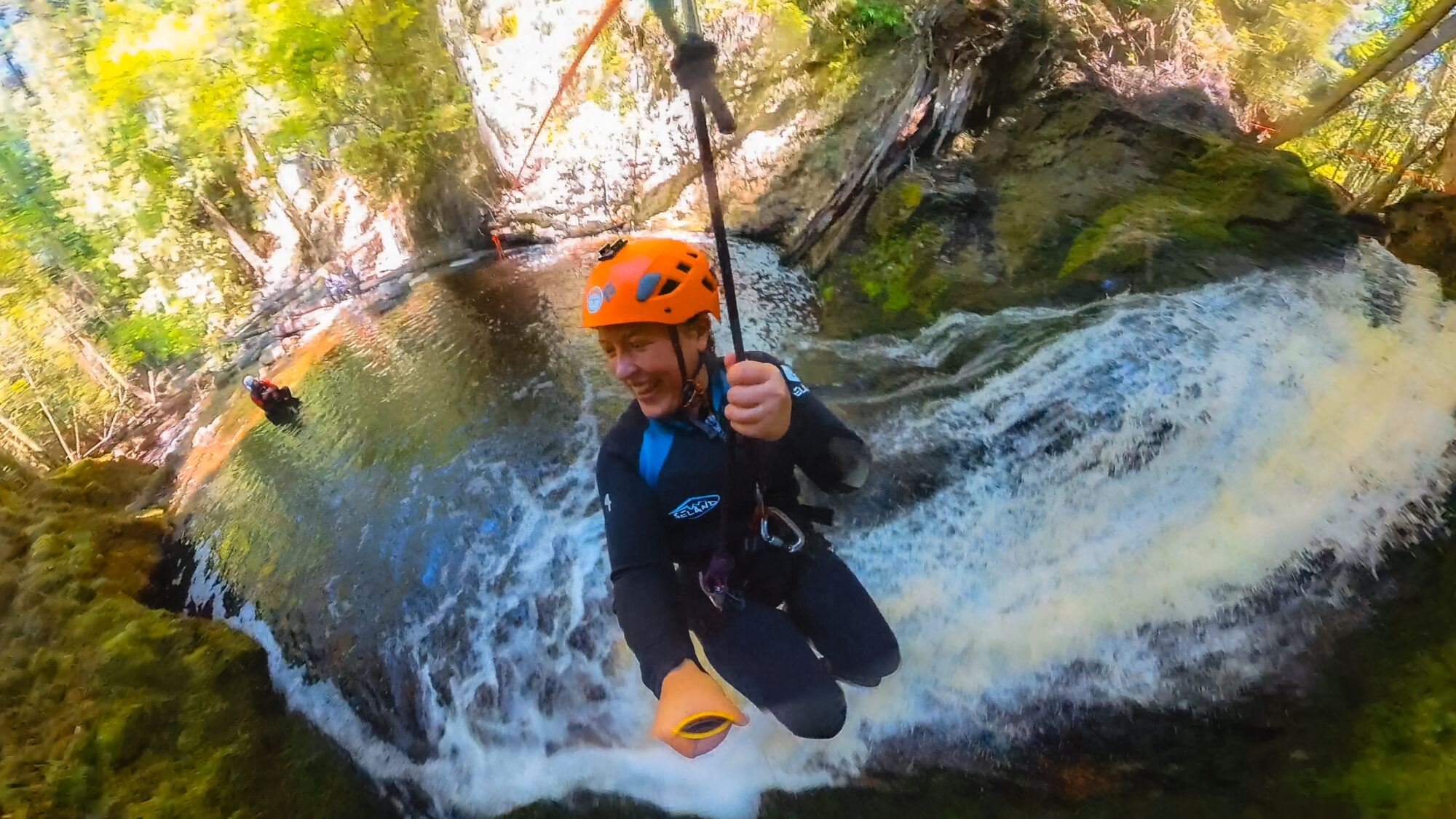 A woman ziplines down a waterfall in a canyon