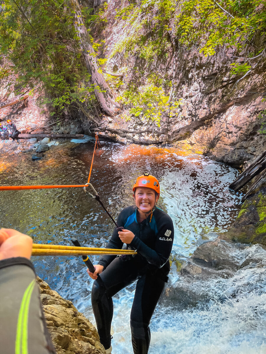 Women smiles at the camera while hanging from a zipline in a canyoning course