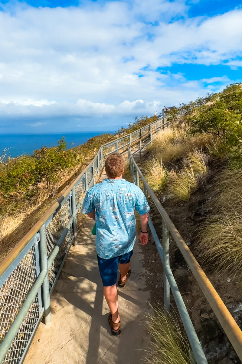 Man walking along a fenced and paved trail.