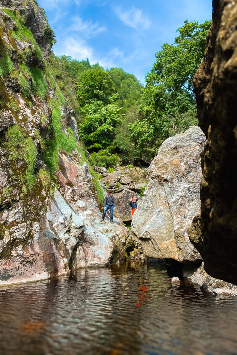 Two men at the far end of a pool surrounded by rocks.