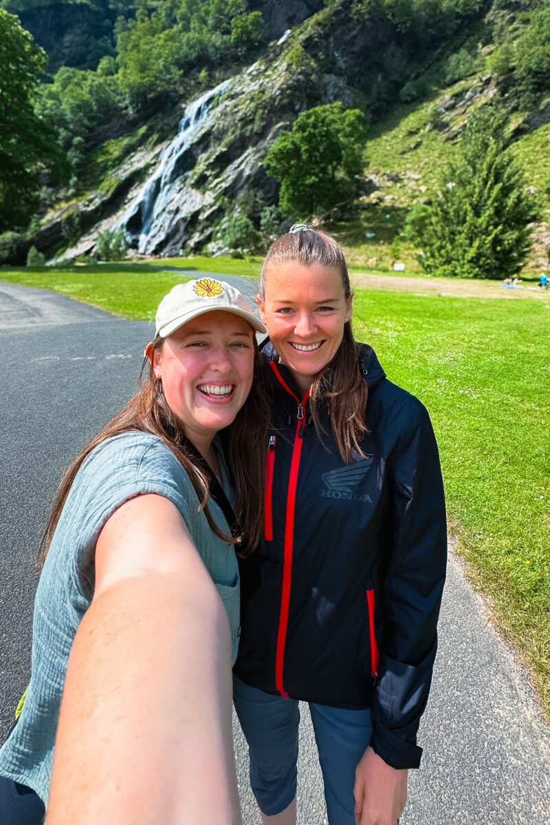 Selfie of two women standing on a paved trail in front of Powerscourt Waterfall.