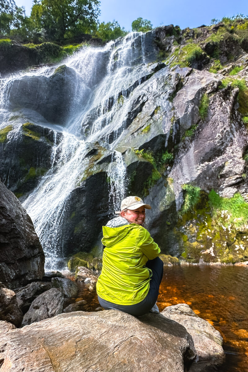 Woman sitting at the base of a large waterfall in Ireland.