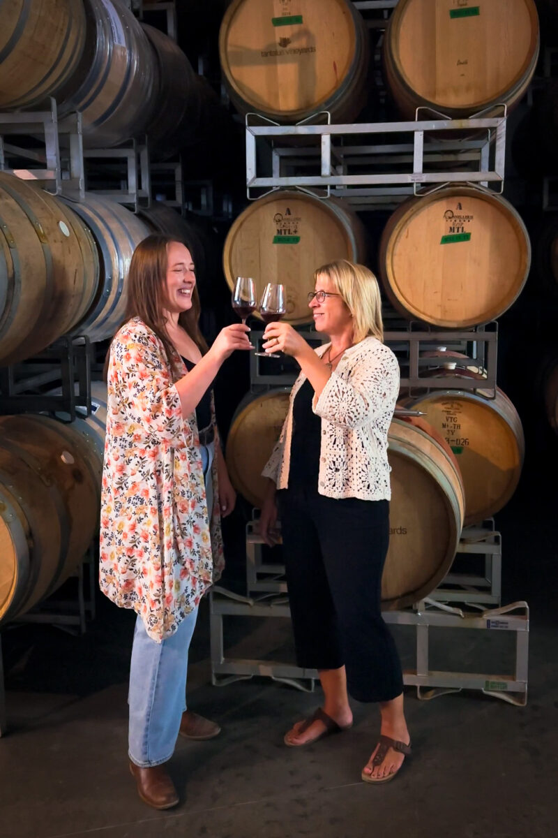 Two woman cheersing in front of wine barrels at Tantalus Vineyards in Kelowna.