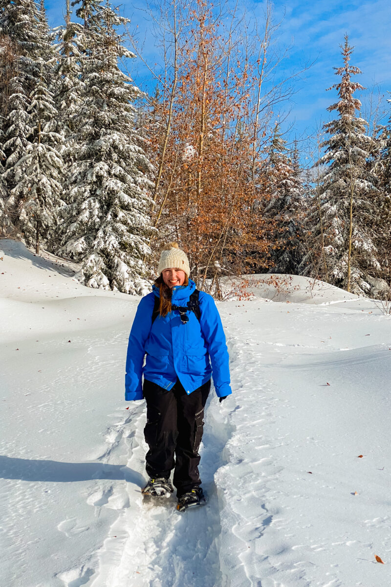 Woman in blue jacket snowshoes through deep snow