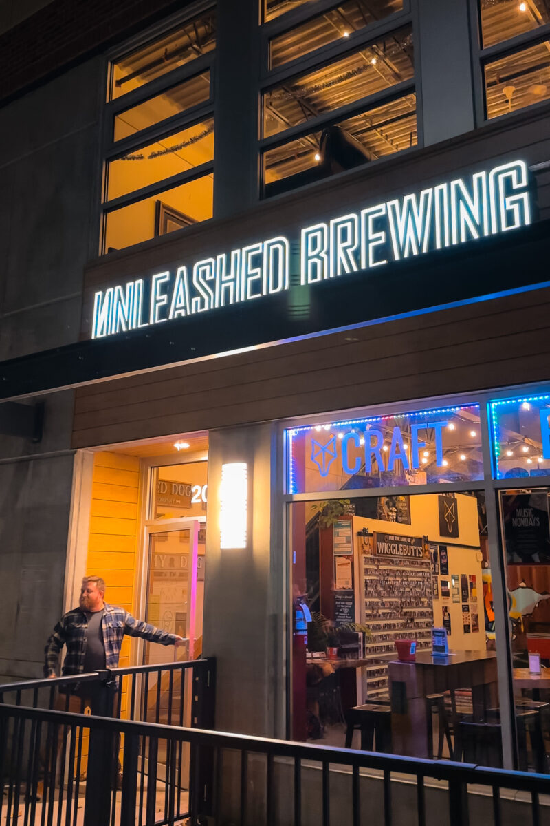 Man holds open a door for a brewery called Unleashed Brewing