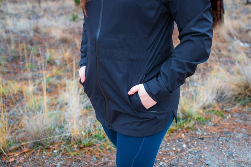 Woman with hands in pockets of a black rain jacket.
