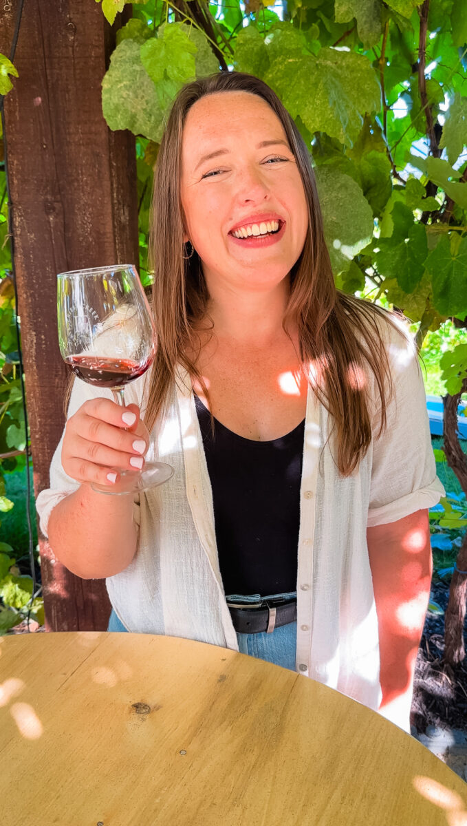 A woman smiling and holding a wine glass at Priest Creek Winery.