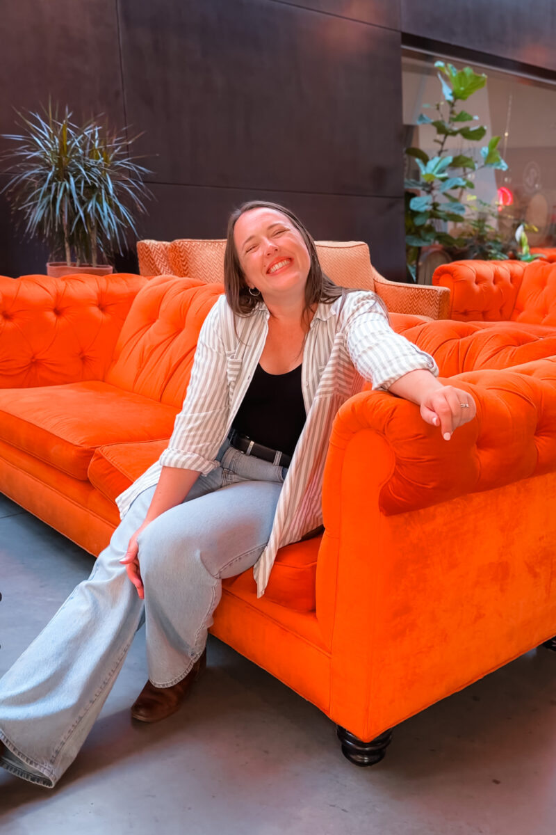 A young woman sitting on an orange counch.