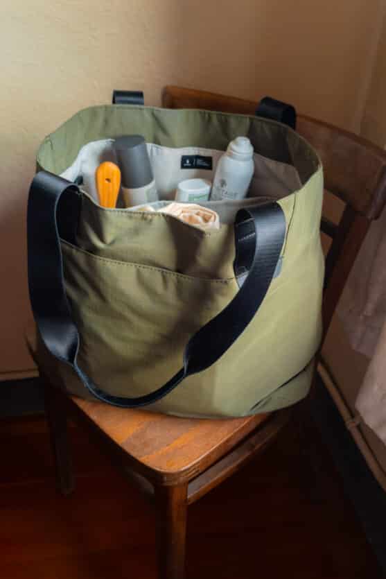 Large ALPAKA tote bag standing upright on chair in a hotel with gear inside