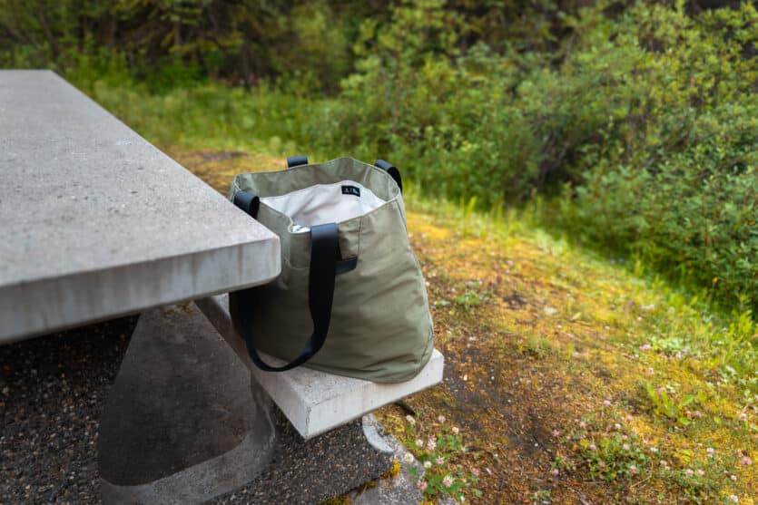 ALPAKA Elements Tote 20L in dark green sitting upright on picnic table during camping trip