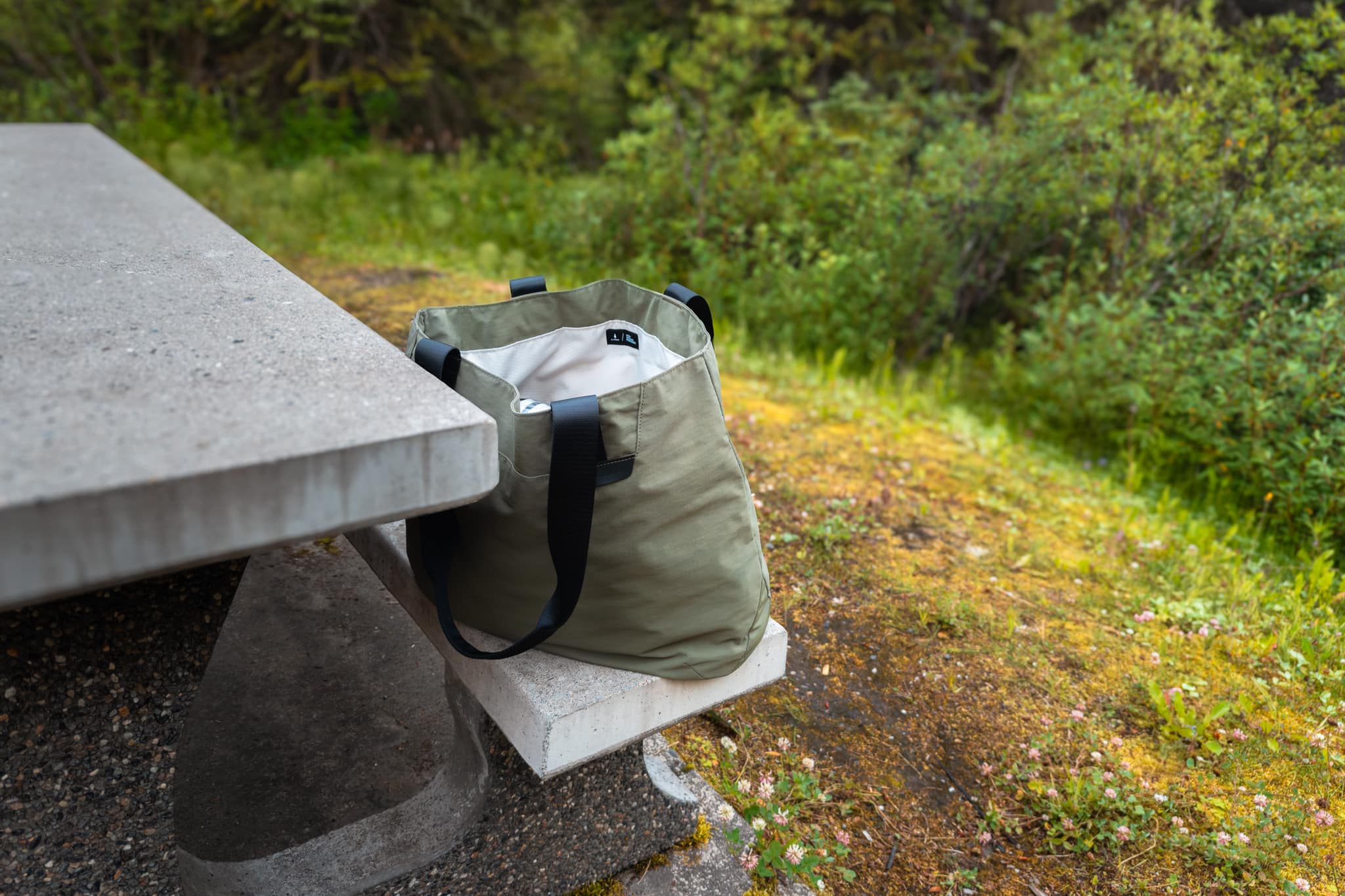 ALPAKA Elements Tote 20L in dark green sitting upright on picnic table during camping trip